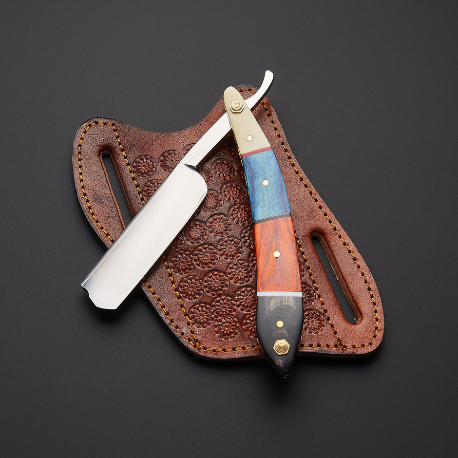 A folding straight razor with a colorful wood and resin handle, displayed with its brown embossed leather sheath on a dark gray background.