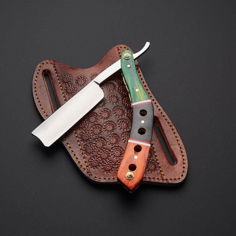 A folding pocket knife with a green and orange wood handle is displayed next to its brown leather sheath on a dark gray background. The sheath features an embossed floral pattern.