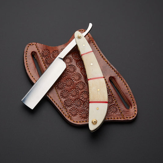 A straight razor with a cream-colored bone handle and red stripes, resting on its brown tooled leather sheath against a dark gray background.