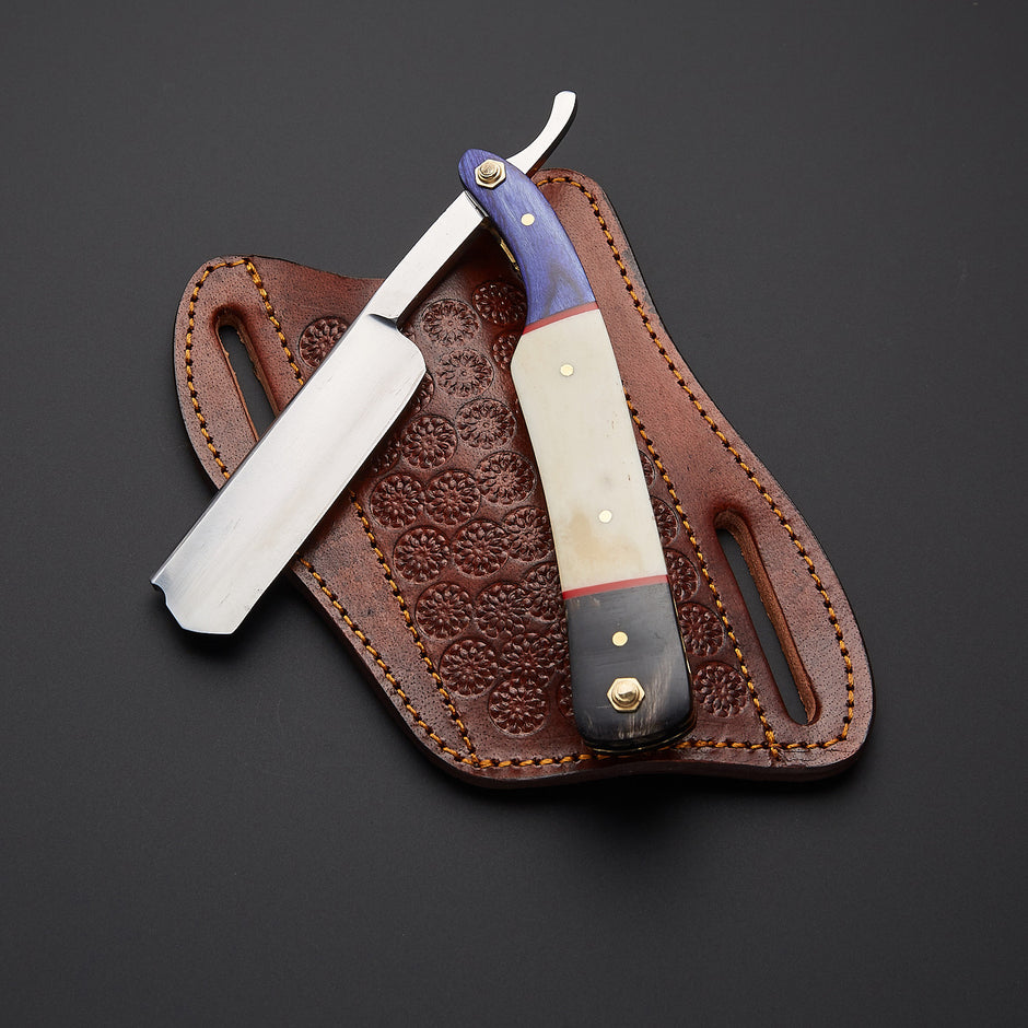 A straight razor with a cream and purple handle rests on a brown embossed leather sheath against a dark gray background.