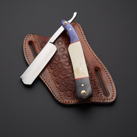 A straight razor with a cream and purple handle rests on a brown embossed leather sheath against a dark gray background.